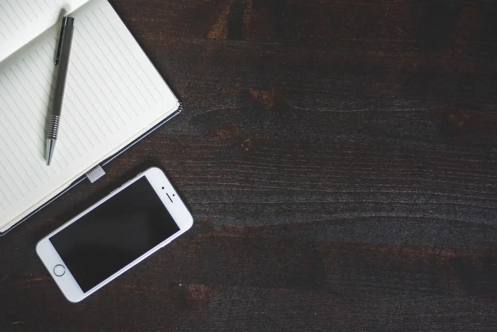 Smartphone, notebook, and pen on a dark wooden desk