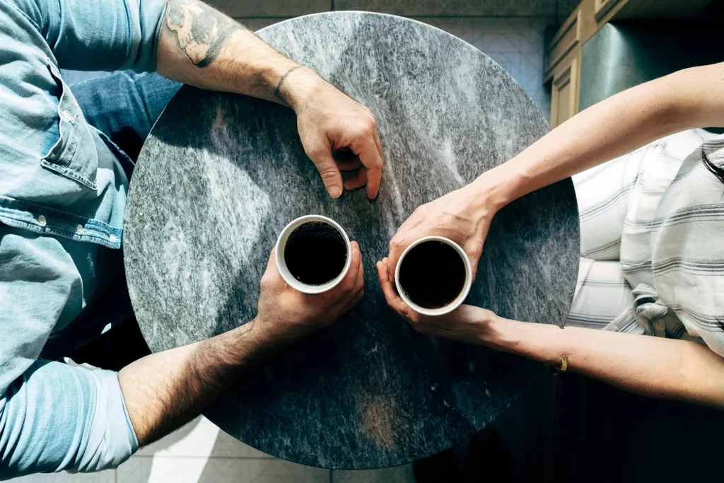 Two people holding cups of coffee across a small round café table, seen from above