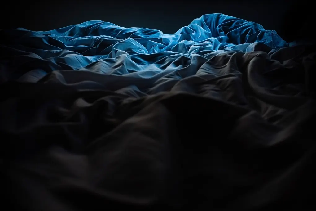 Rumpled blue bedsheets in a dark bedroom