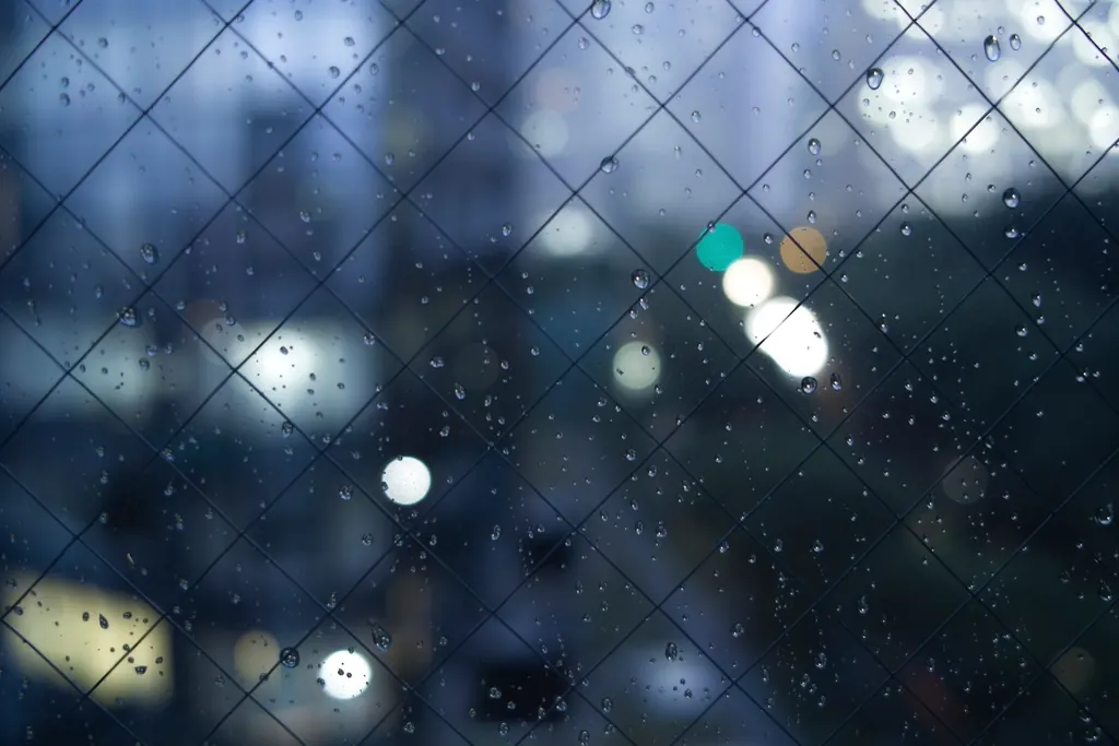 Raindrops on a window with blurred city lights behind it at night