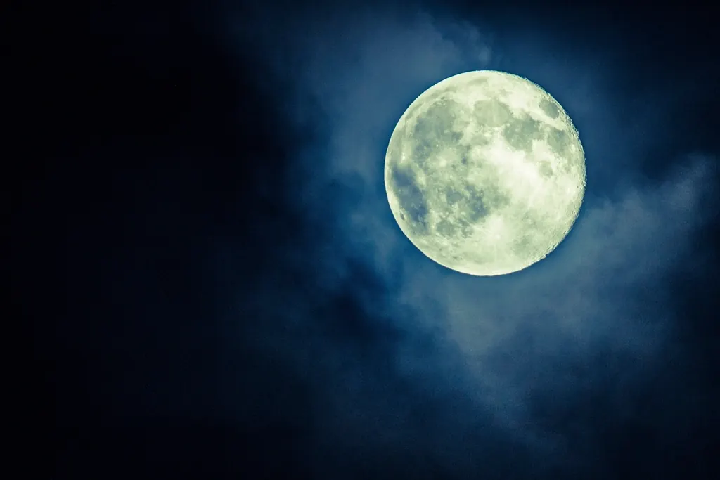 Full moon glowing through clouds in a dark blue night sky